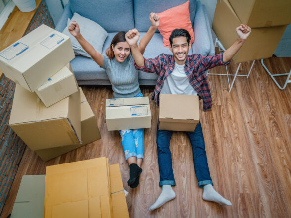 Top view Asian young couple are glad after successfull packing the cardboard box for moving in new house, Helping relocate and joshing together, Moving and House Hunting concept, selective focus